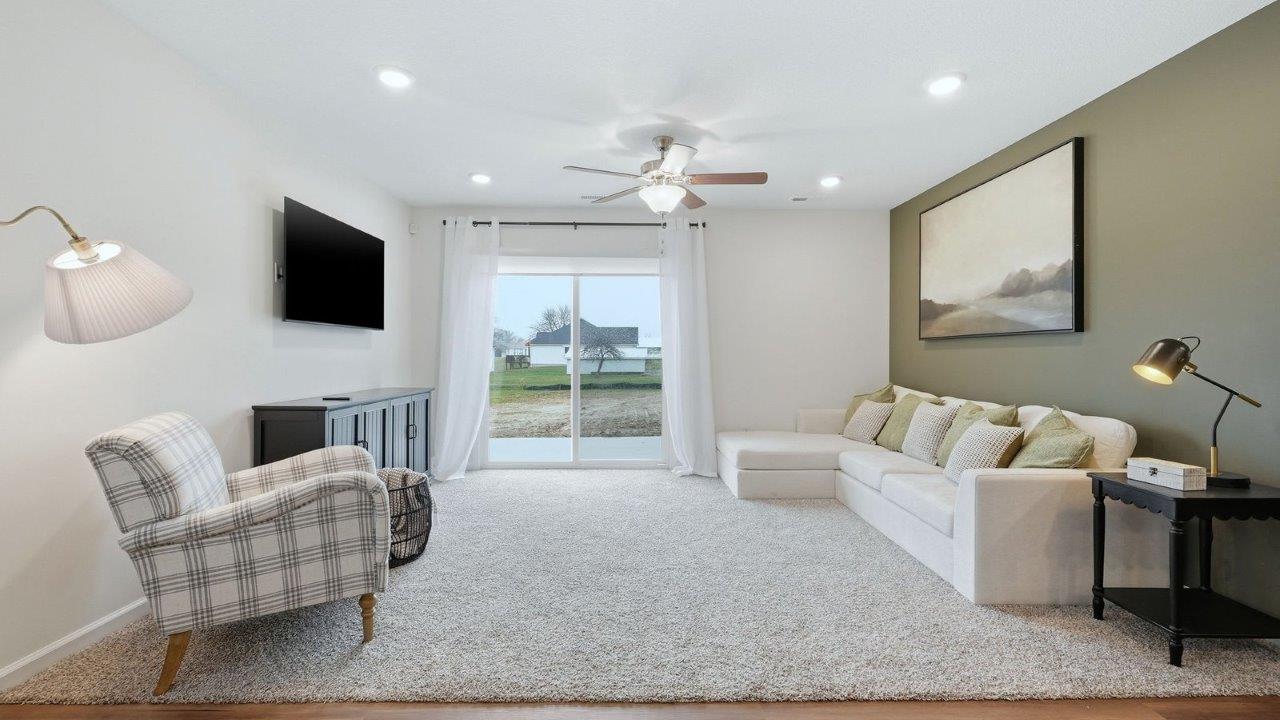 thunderhawk model home elm plan open concept living room with beige carpet and white and green walls with sliding glass door to backyard patio