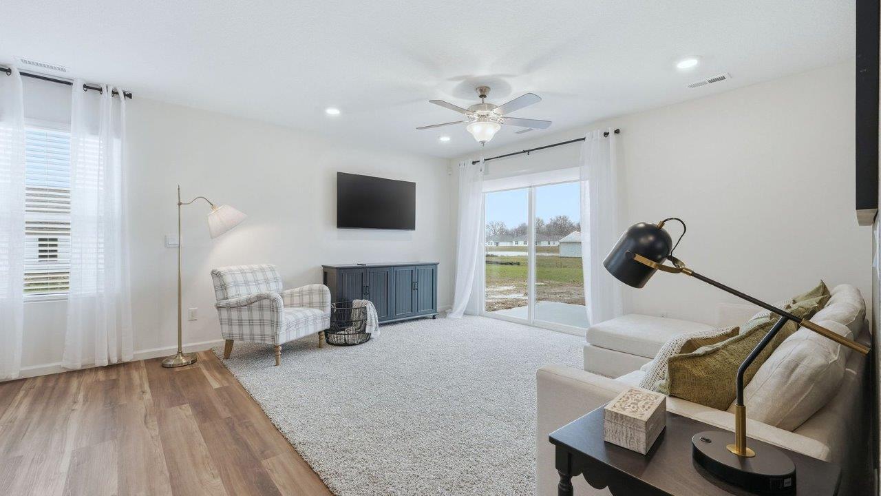 thunderhawk model home elm plan open concept living room with beige carpet and white and green walls with sliding glass door to backyard patio