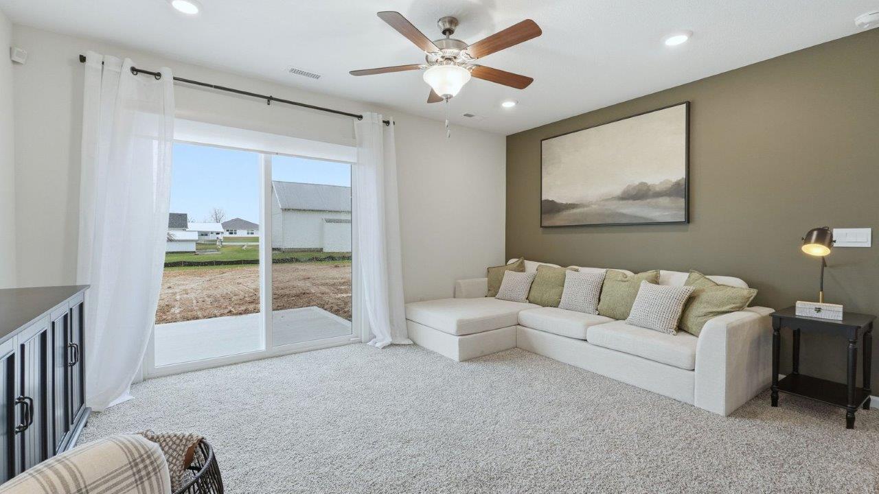 thunderhawk model home elm plan open concept living room with beige carpet and white and green walls with sliding glass door to backyard patio