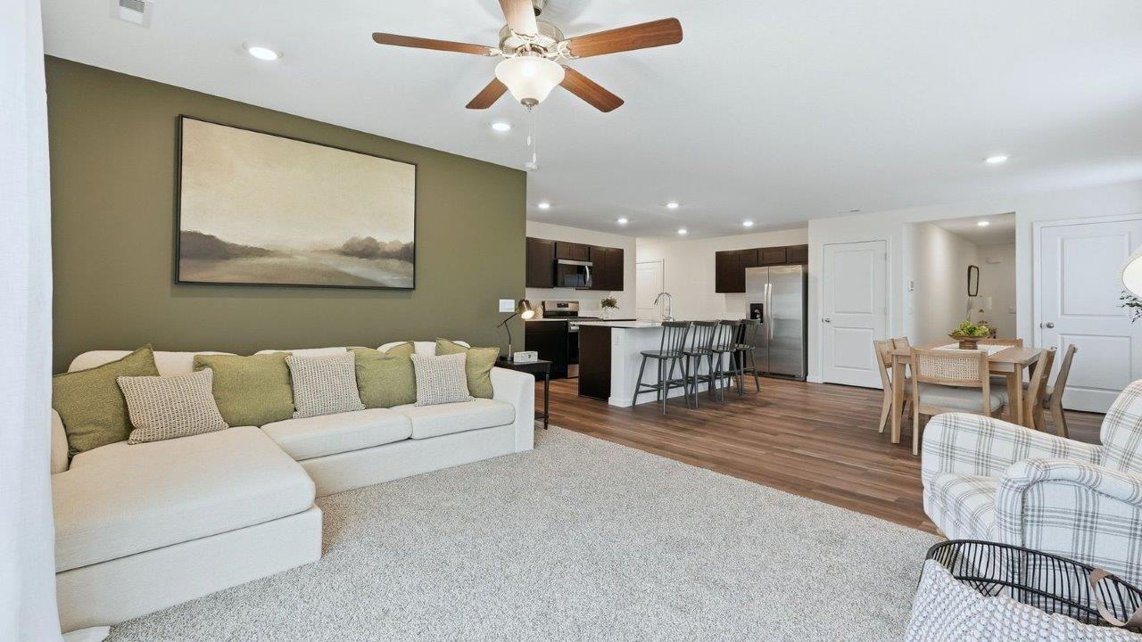 thunderhawk model home elm plan open concept living room with beige carpet and white and green walls with sliding glass door to backyard patio