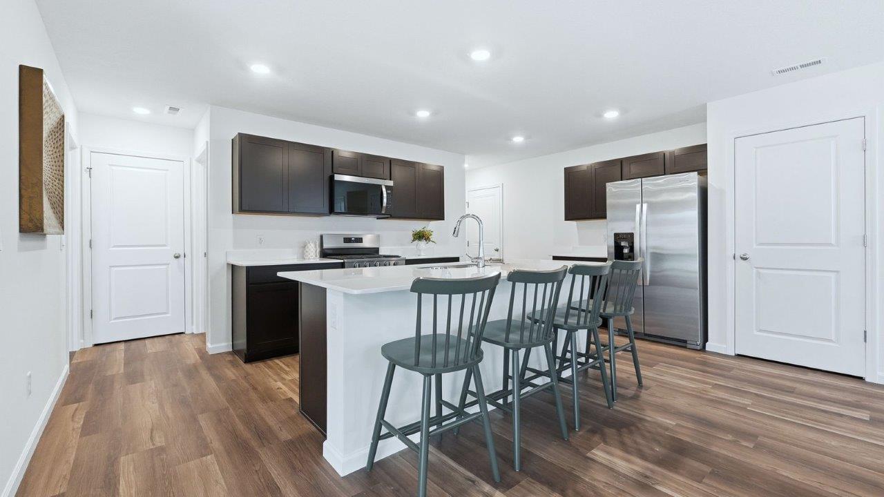 thunderhawk model home elm plan kitchen with sarsaparilla shaker cabinets, quartz countertops, center island with bar seating, pantry, and stainless steel appliances