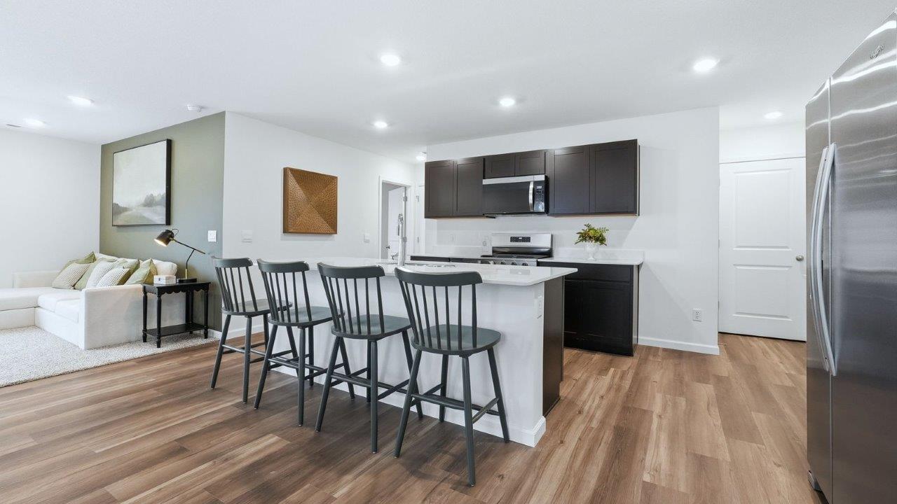 thunderhawk model home elm plan kitchen with sarsaparilla shaker cabinets, quartz countertops, center island with bar seating, pantry, and stainless steel appliances