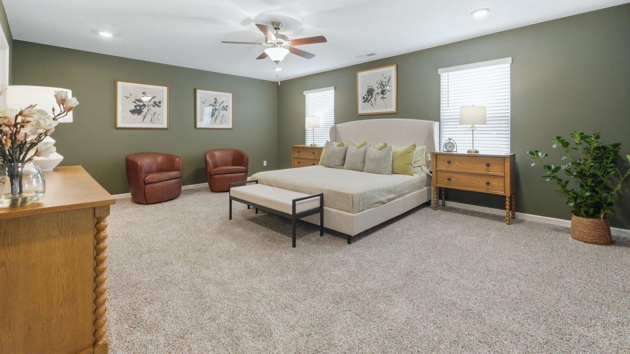 thunderhawk elm model home primary bedroom with carpet green walls and ensuite bathroom and walk in closet