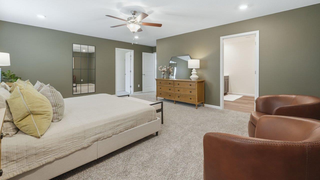 thunderhawk elm model home primary bedroom with carpet green walls and ensuite bathroom and walk in closet