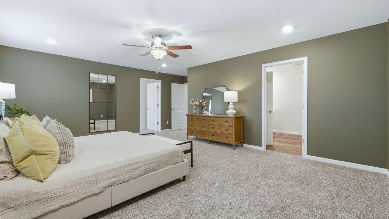 thunderhawk model home elm plan primary bedroom with beige carpet flooring, sage green walls, 2 large windows, with space for seating and ensuite bath and closet