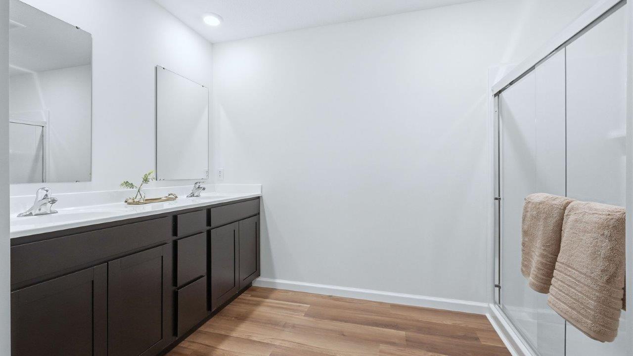 thunderhawk model home elm plan primary ensuite bathroom with dual vanity sinks with sarsaparilla cabinetry, mohawk lvp flooring, walk-in fiberglass shower, and private water room