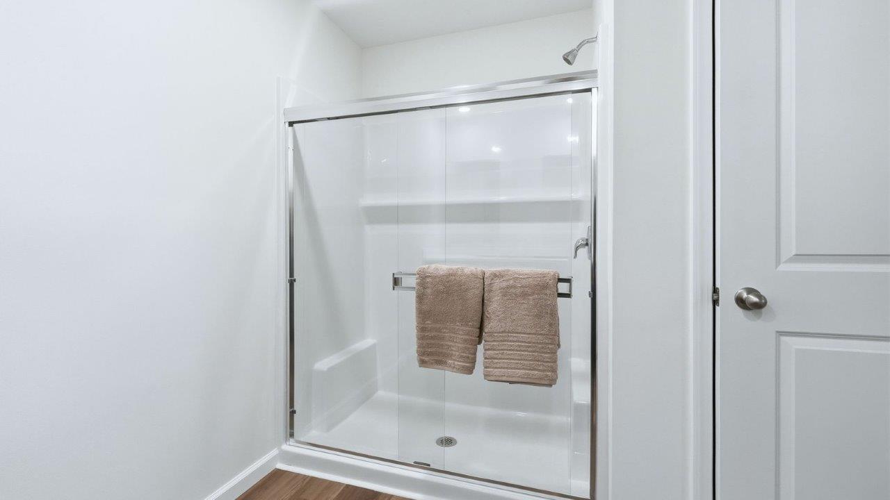 thunderhawk model home elm plan primary ensuite bathroom with dual vanity sinks with sarsaparilla cabinetry, mohawk lvp flooring, walk-in fiberglass shower, and private water room