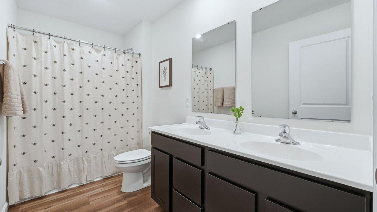 thunderhawk model home elm plan full bathroom with dual vanity sinks, sarsaparilla cabinets, white marble counters, and fiberglass tub shower