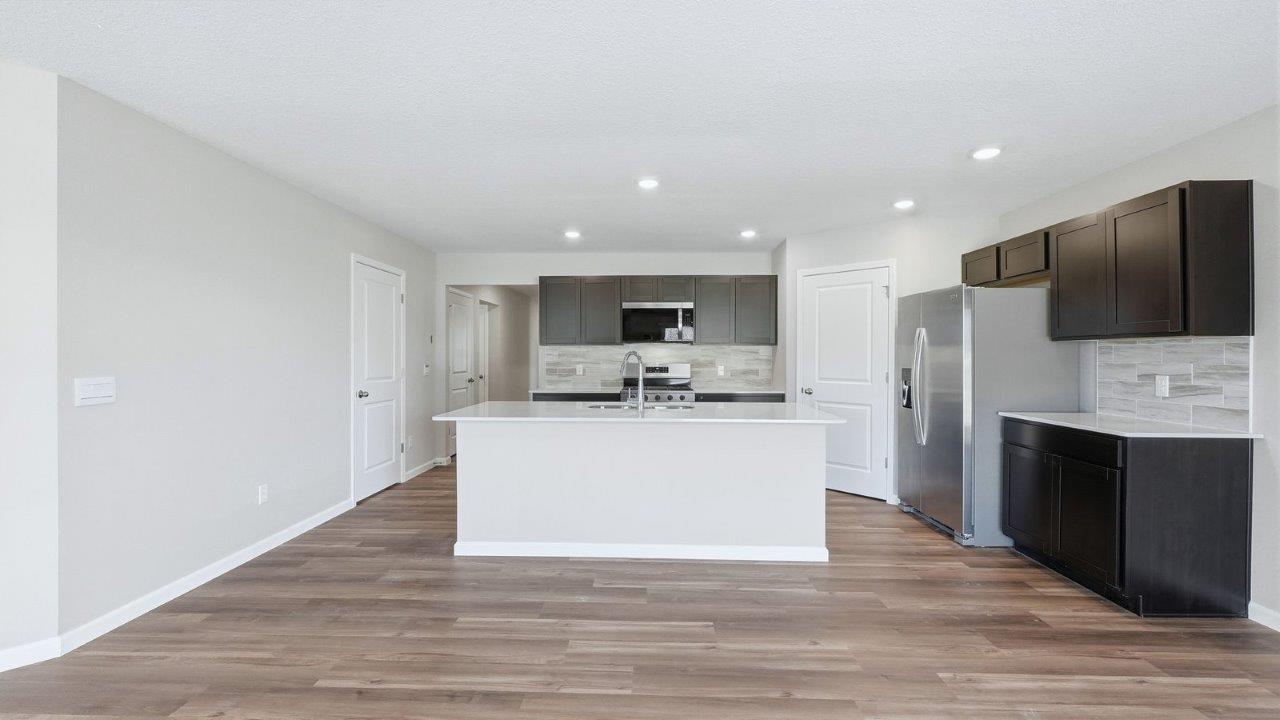 kitchen with sarsaparilla cabinets, lvp, quartz counters, corner pantry, stainless steel appliances, and center island with bar seating