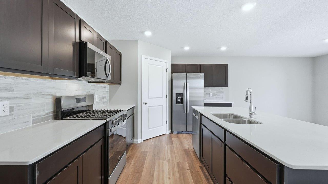 kitchen with sarsaparilla cabinets, lvp, quartz counters, corner pantry, stainless steel appliances, and center island with bar seating