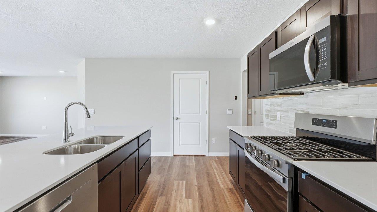 kitchen with sarsaparilla cabinets, lvp, quartz counters, corner pantry, stainless steel appliances, and center island with bar seating