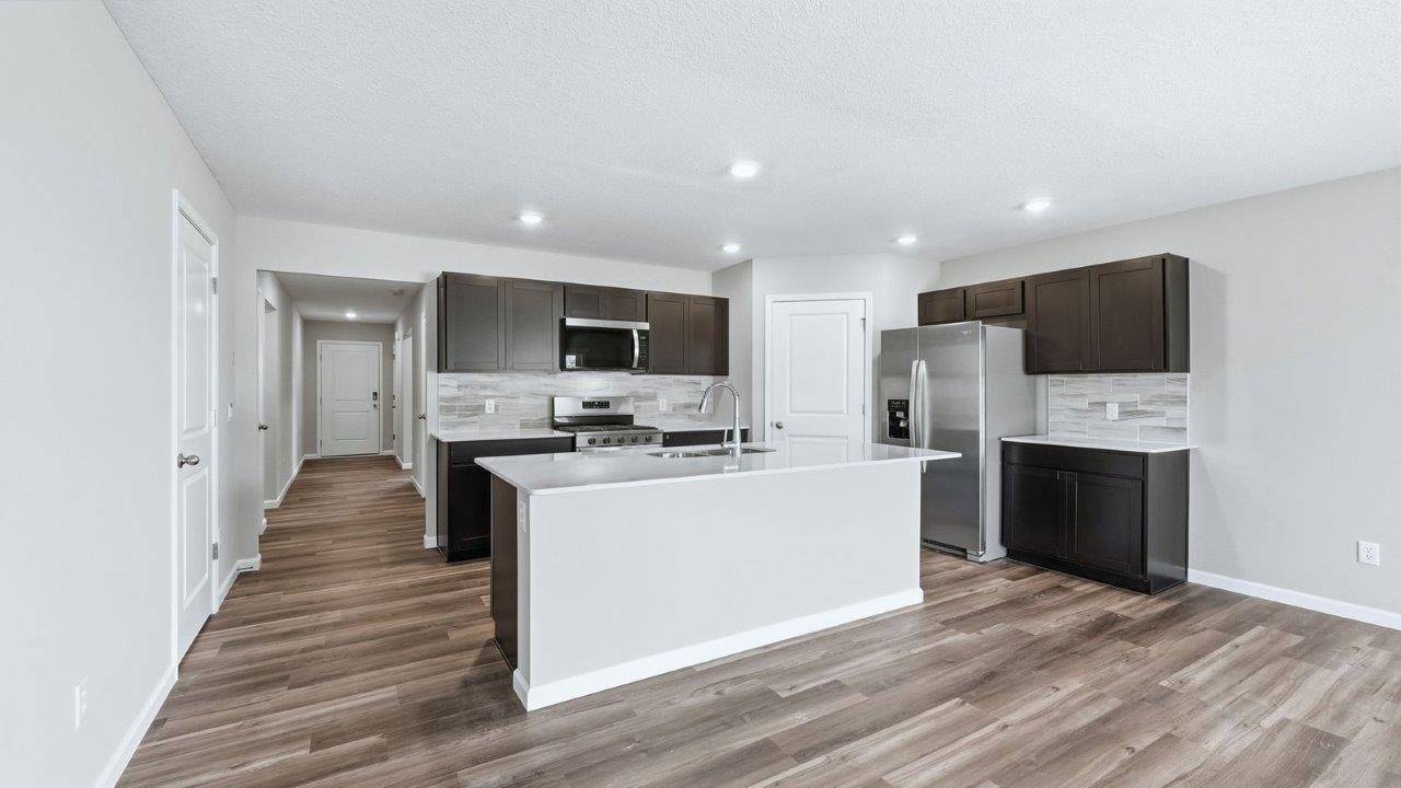 kitchen with sarsaparilla cabinets, lvp, quartz counters, corner pantry, stainless steel appliances, and center island with bar seating