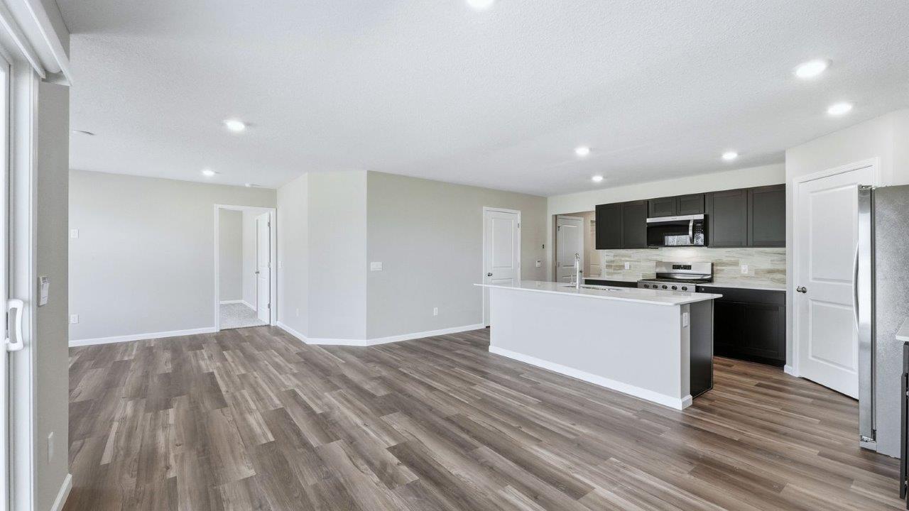 kitchen with sarsaparilla cabinets, lvp, quartz counters, corner pantry, stainless steel appliances, and center island with bar seating