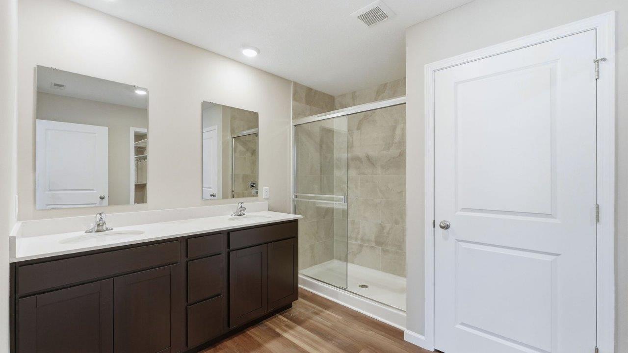 primary ensuite bathroom with dual sinks, ceramic tile shower, and private toilet