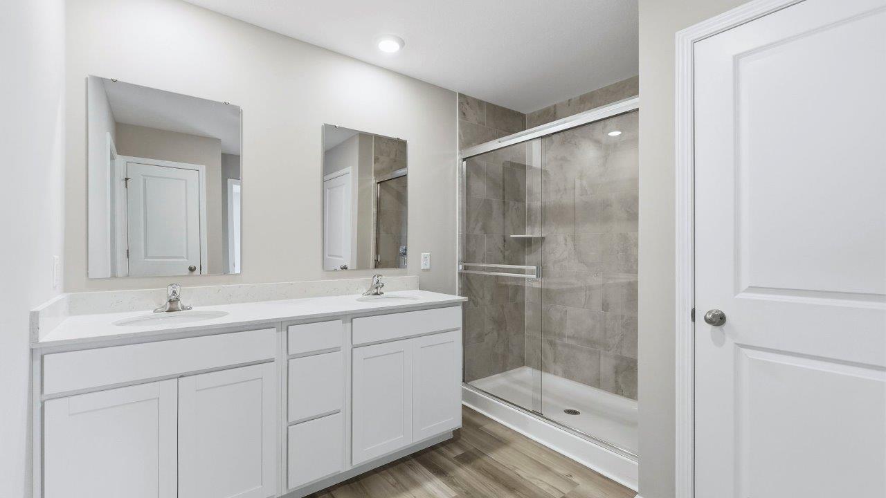 primary bath with dual sinks and tile shower