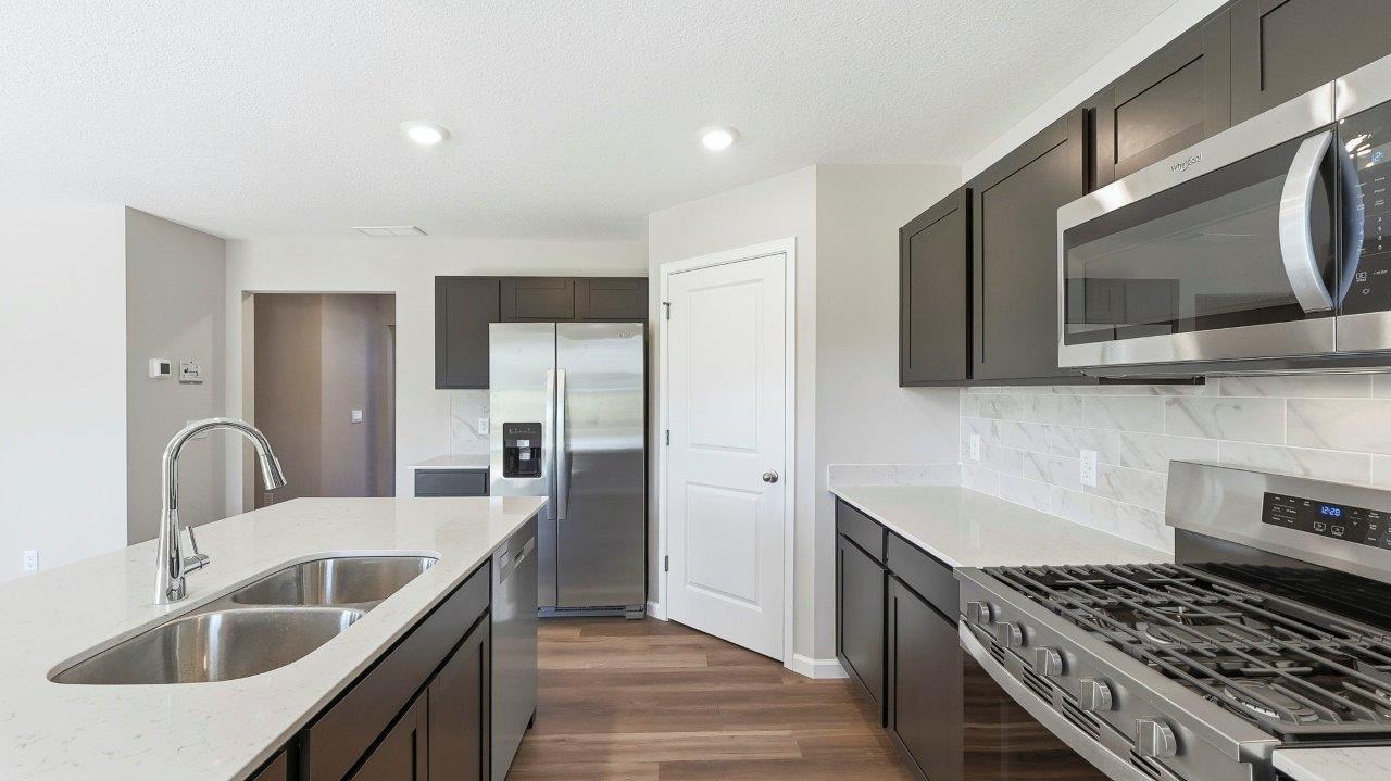 kitchen with sarsaparilla cabinets, stainless steel appliances, corner pantry, and center island with quartz counters