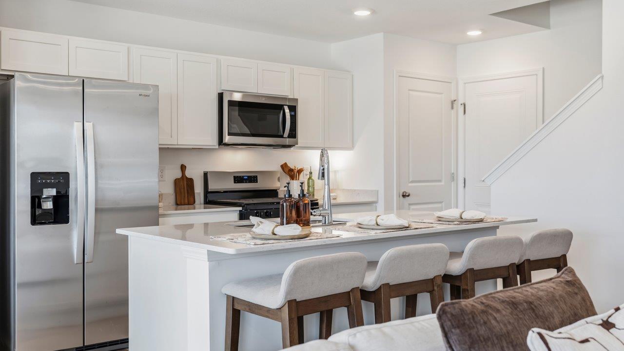Whispering Pines Pattison Model - kitchen with white cabinets, quartz countertops, center island with bar seating, stainless steel appliances, and pantry