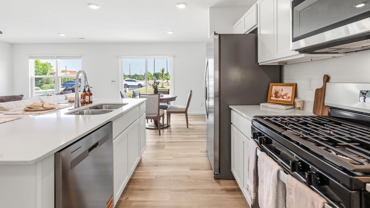 Whispering Pines Pattison Model - kitchen with white cabinets, quartz countertops, center island with bar seating, stainless steel appliances, and pantry