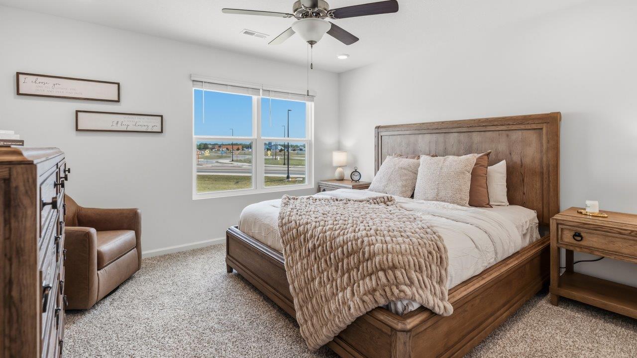 Whispering Pines Pattison Model - primary bedroom with carpet flooring, ceiling fan, white walls, 2 windows, and ensuite bathroom and walk in closet
