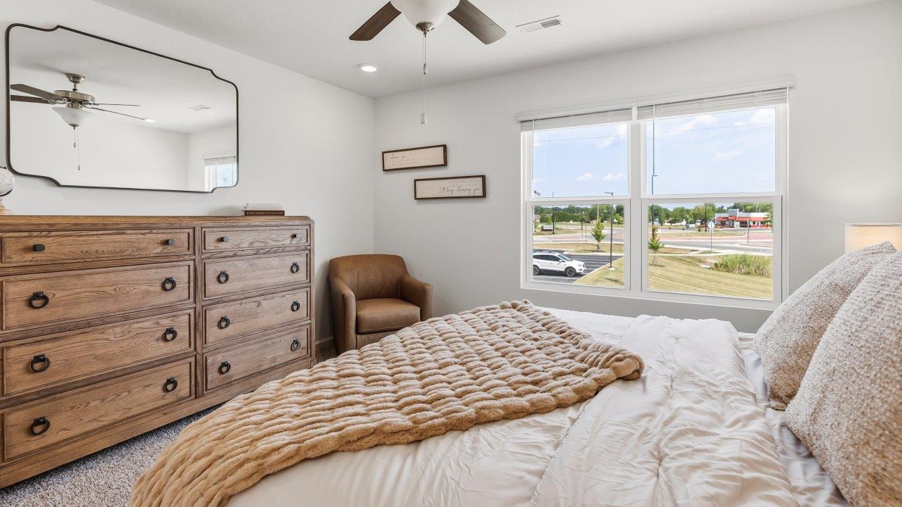 Whispering Pines Pattison Model - primary bedroom with carpet flooring, ceiling fan, white walls, 2 windows, and ensuite bathroom and walk in closet