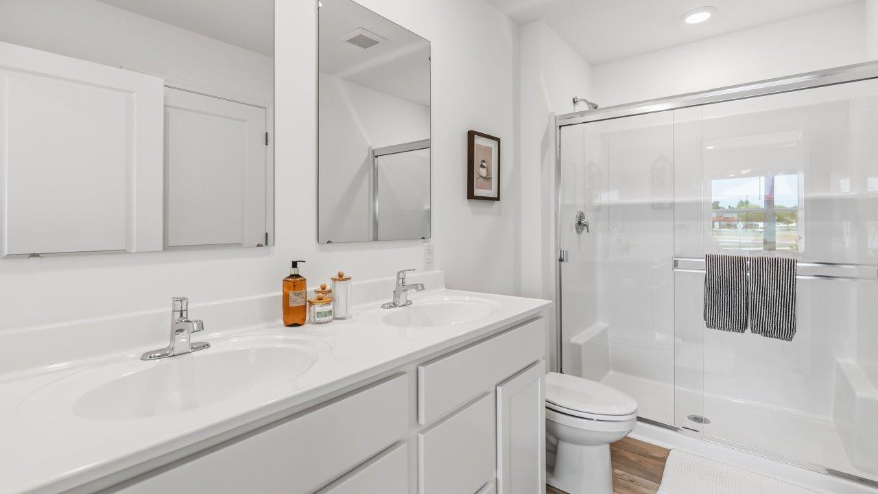 Whispering Pines Pattison Model - primary bedroom ensuite bathroom with dual sinks, white cabinetry, cultures marble countertops, and walk in shower