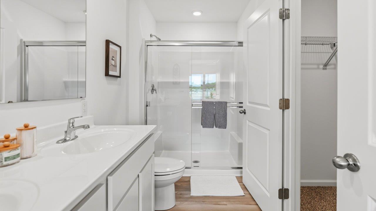 Whispering Pines Pattison Model - primary bedroom ensuite bathroom with dual sinks, white cabinetry, cultures marble countertops, and walk in shower