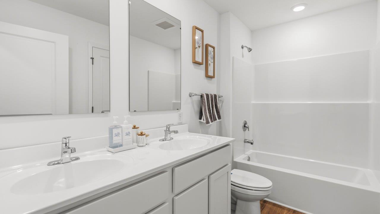 Whispering Pines Pattison Model - full bathroom with dual sink vanity, white cabinetry, lvp flooring, and fiberglass tub shower