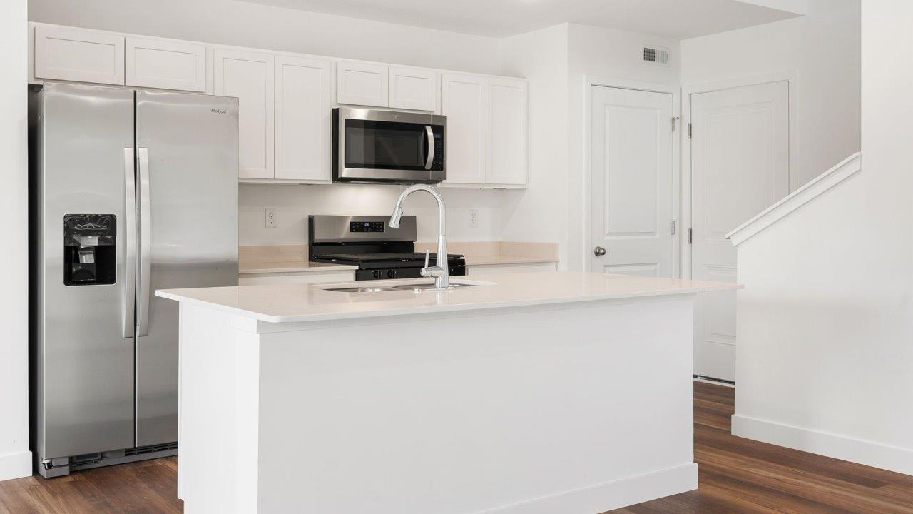 whispering pines portsmouth - kitchen with white cabinets, stainless steel appliances, quartz countertops, center island, and pantry
