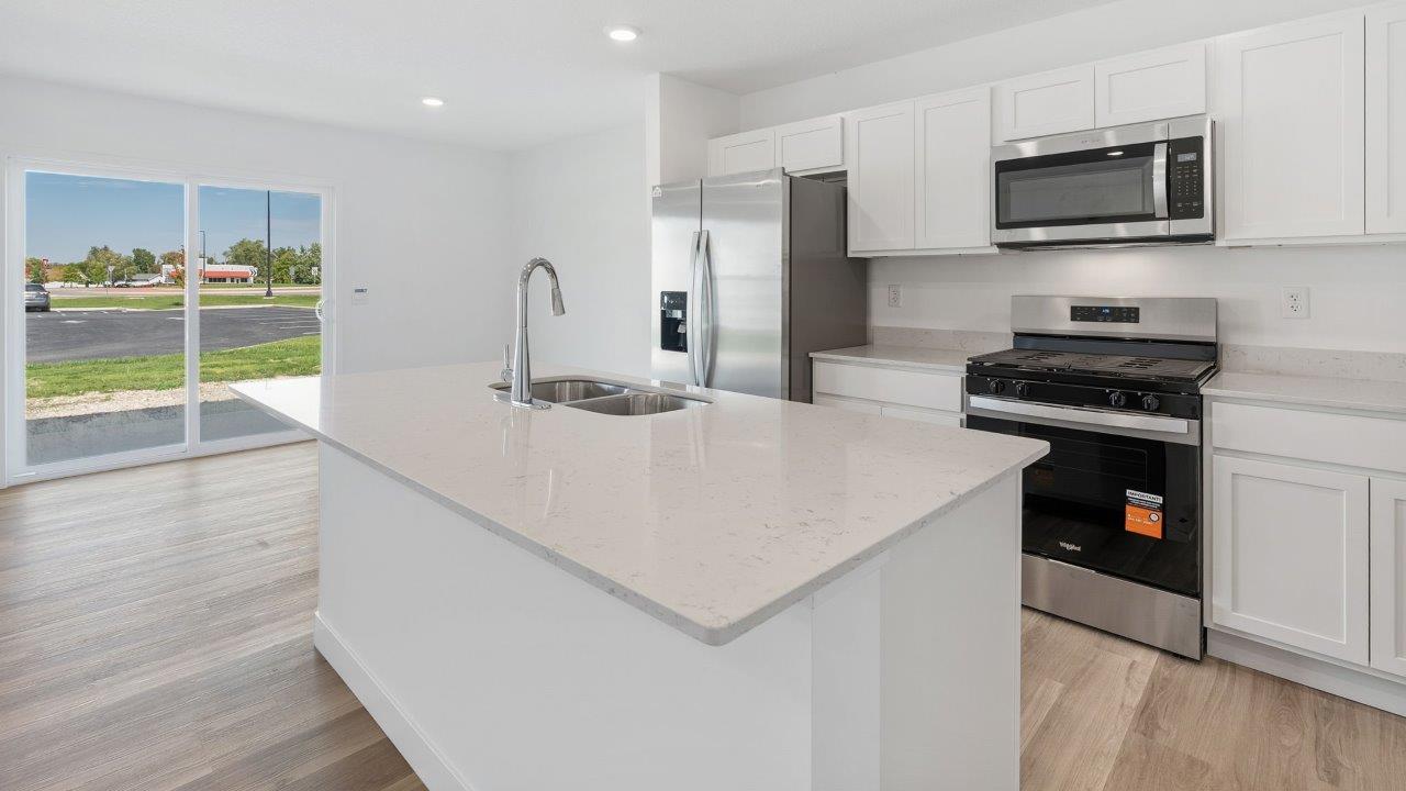 whispering pines portsmouth kitchen with white shaker cabinets, quartz countertops, stainless steel appliances, pantry, moahwk lvp flooring, white walls, and center island with room for bar seating