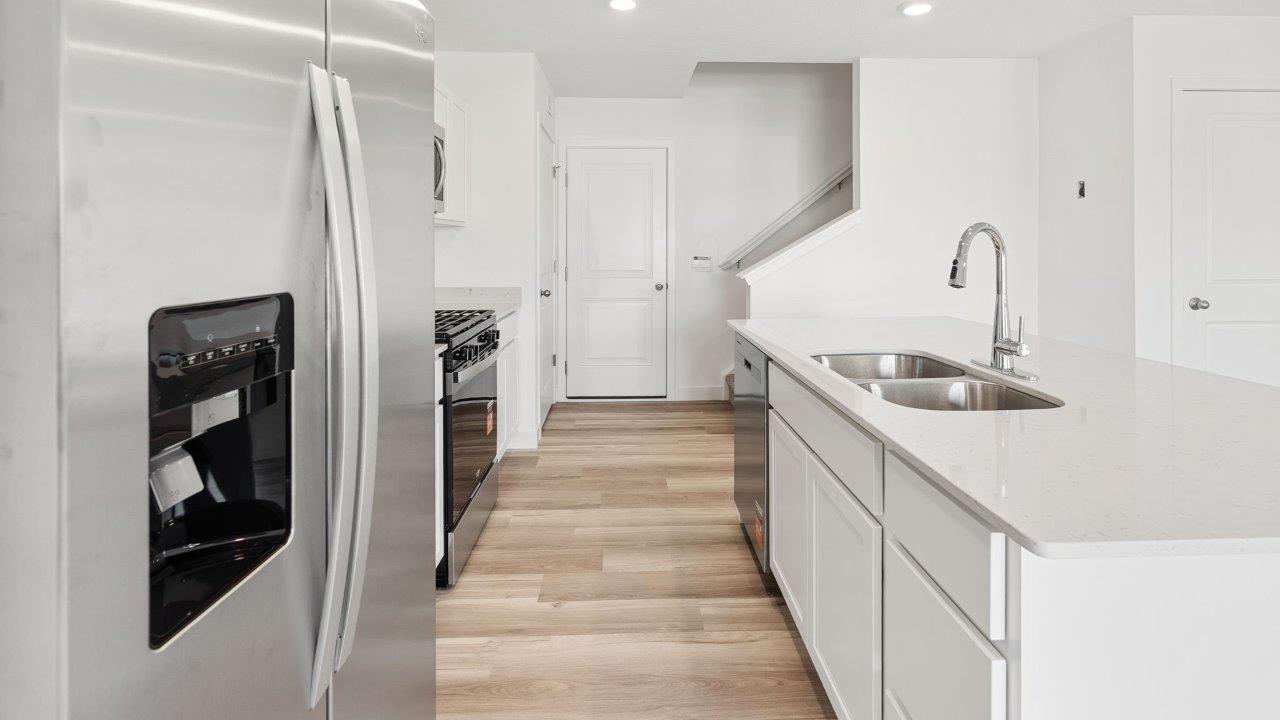 whispering pines portsmouth kitchen with white shaker cabinets, quartz countertops, stainless steel appliances, pantry, moahwk lvp flooring, white walls, and center island with room for bar seating