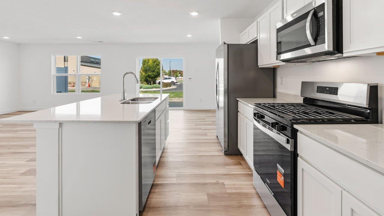 whispering pines portsmouth kitchen with white shaker cabinets, quartz countertops, stainless steel appliances, pantry, moahwk lvp flooring, white walls, and center island with room for bar seating