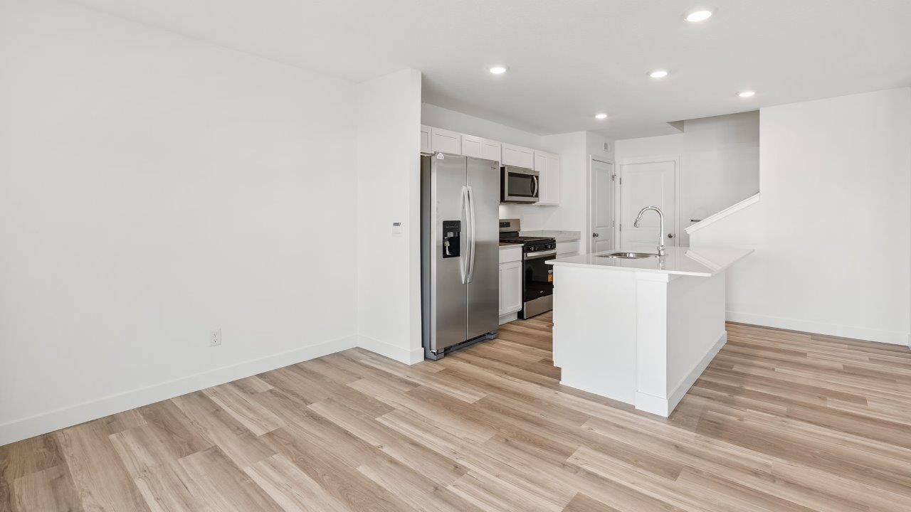 whispering pines portsmouth kitchen with white shaker cabinets, quartz countertops, stainless steel appliances, pantry, moahwk lvp flooring, white walls, and center island with room for bar seating