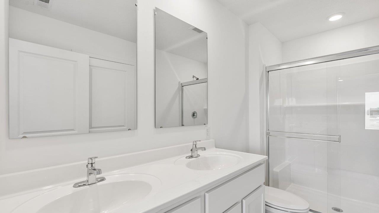 whispering pines portsmouth primary bedroom ensuite bathroom with dual sink vanity, walk in shower, cultured white marble flooring, white cabinets, and mohawk lvp flooring