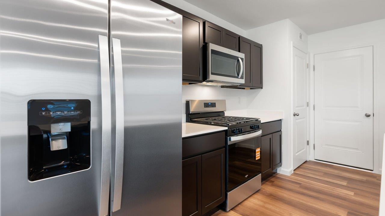 whispering pines portsmouth kitchen with sarsaparilla cabinets, quartz counters, island with bar seating, pantry, and stainless steel appliances