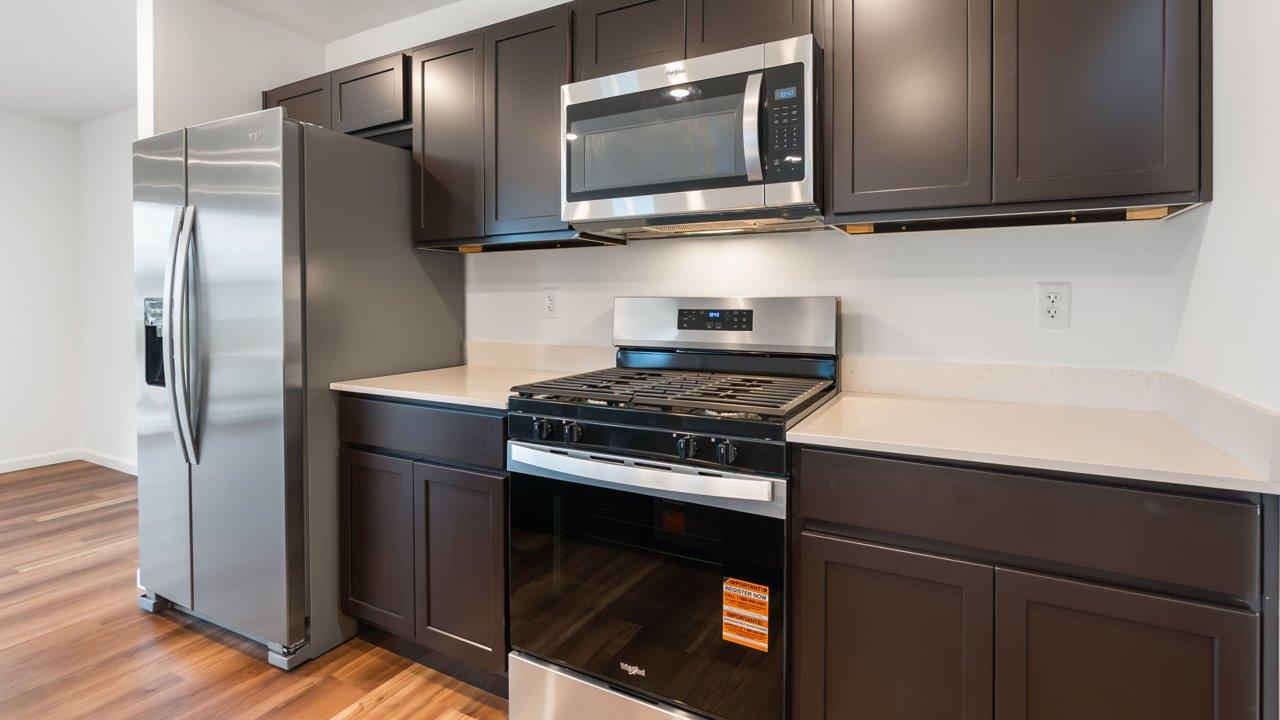 whispering pines portsmouth kitchen with sarsaparilla cabinets, quartz counters, island with bar seating, pantry, and stainless steel appliances