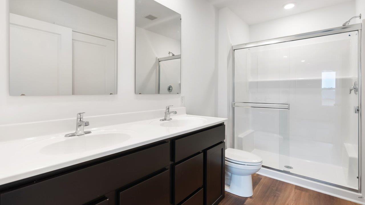 whispering pines portsmouth primary bedroom ensuite bathroom with dual sinks, sarsaparilla cabinets, and walk in shower