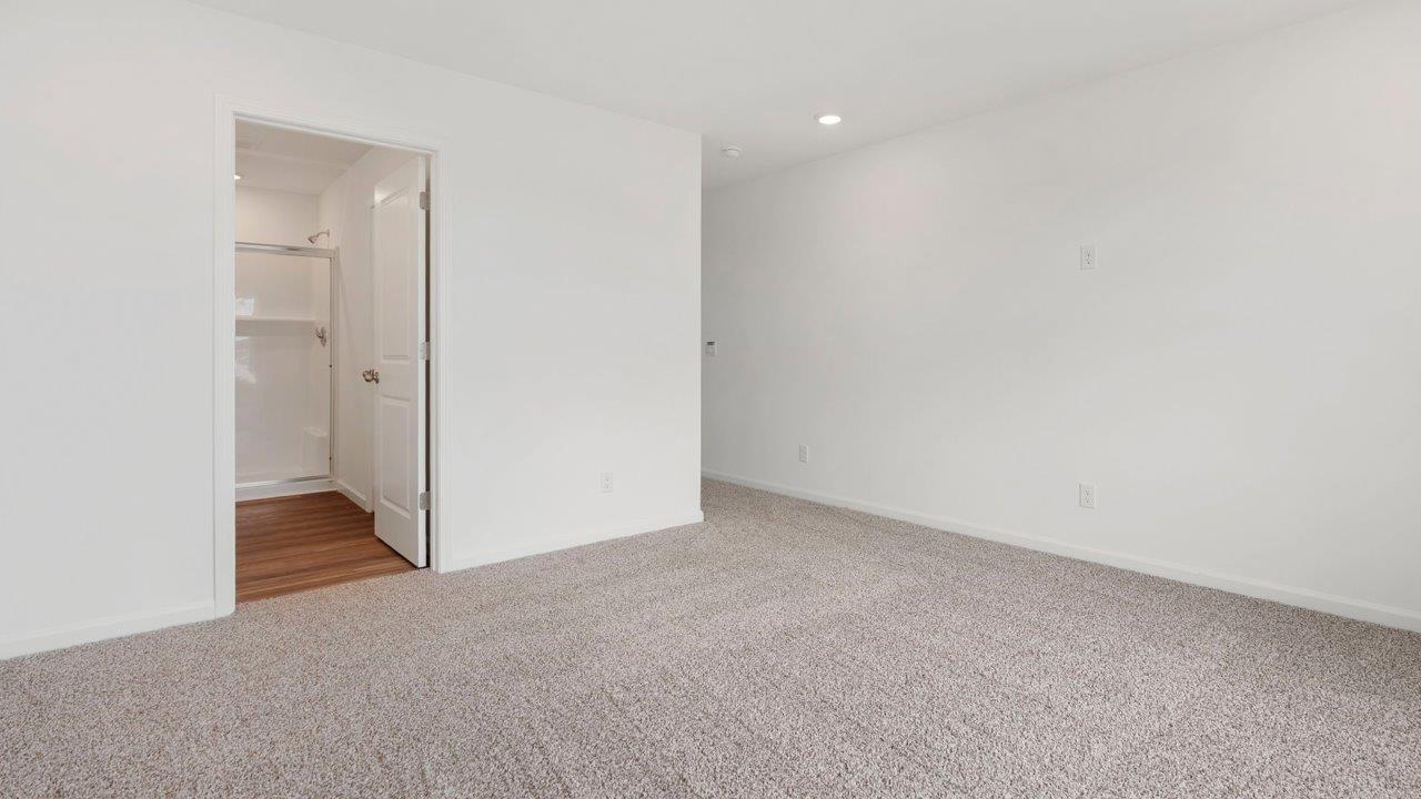 primary bedroom with carpet flooring, white walls, 2 windows, and ensuite bathroom and walk in closet