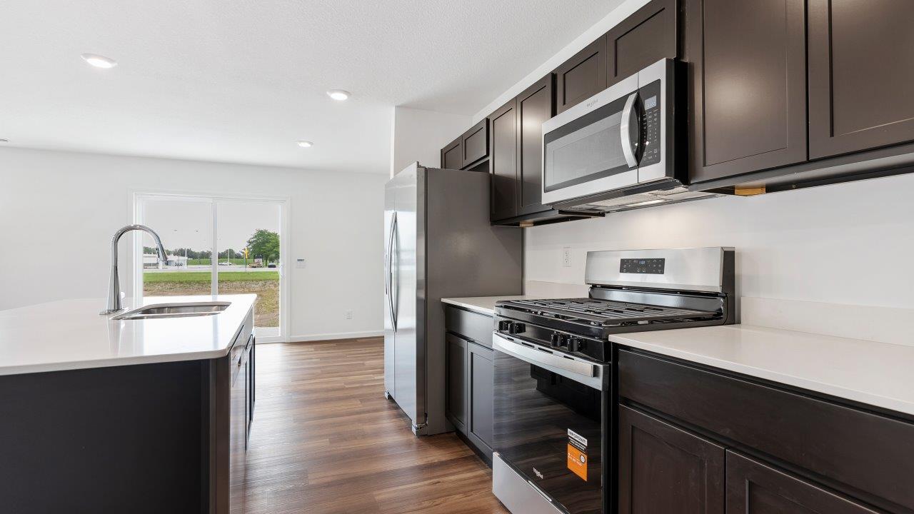 kitchen with sarsaparilla cabinets, quartz countertops, stainless steel appliances, pantry, and island