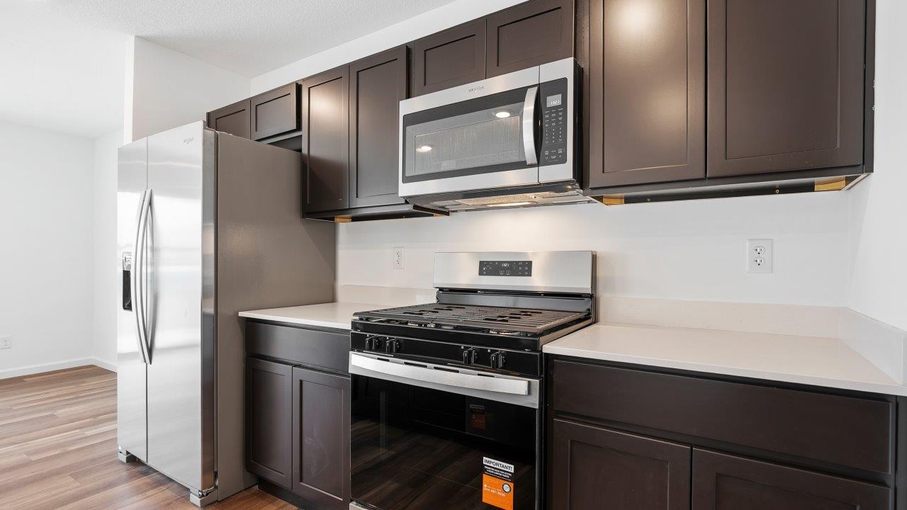 kitchen with sarsaparilla cabinets, quartz countertops, stainless steel appliances, pantry, and island
