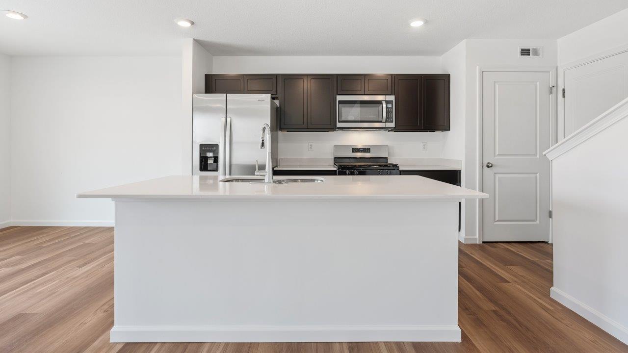 kitchen with sarsaparilla cabinets, quartz countertops, stainless steel appliances, pantry, and island
