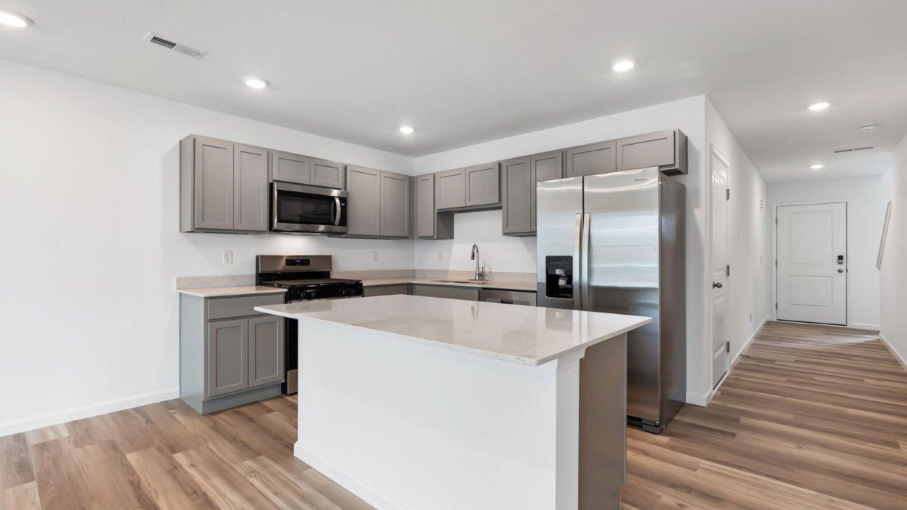 whispering pines pearson kitchen with gray cabinets, quartz countertops, lvp flooring, island with bar seating, and stainless steel appliances