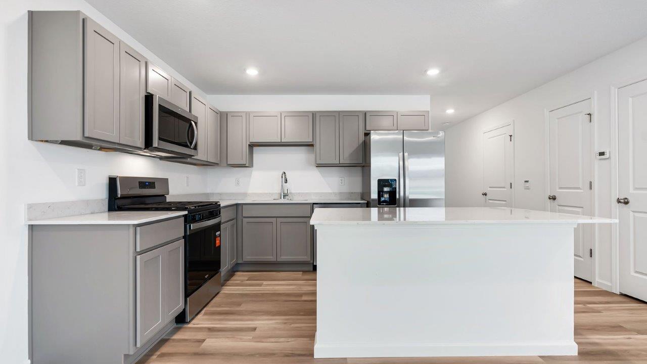 whispering pines pearson kitchen with gray cabinets, quartz countertops, lvp flooring, island with bar seating, and stainless steel appliances