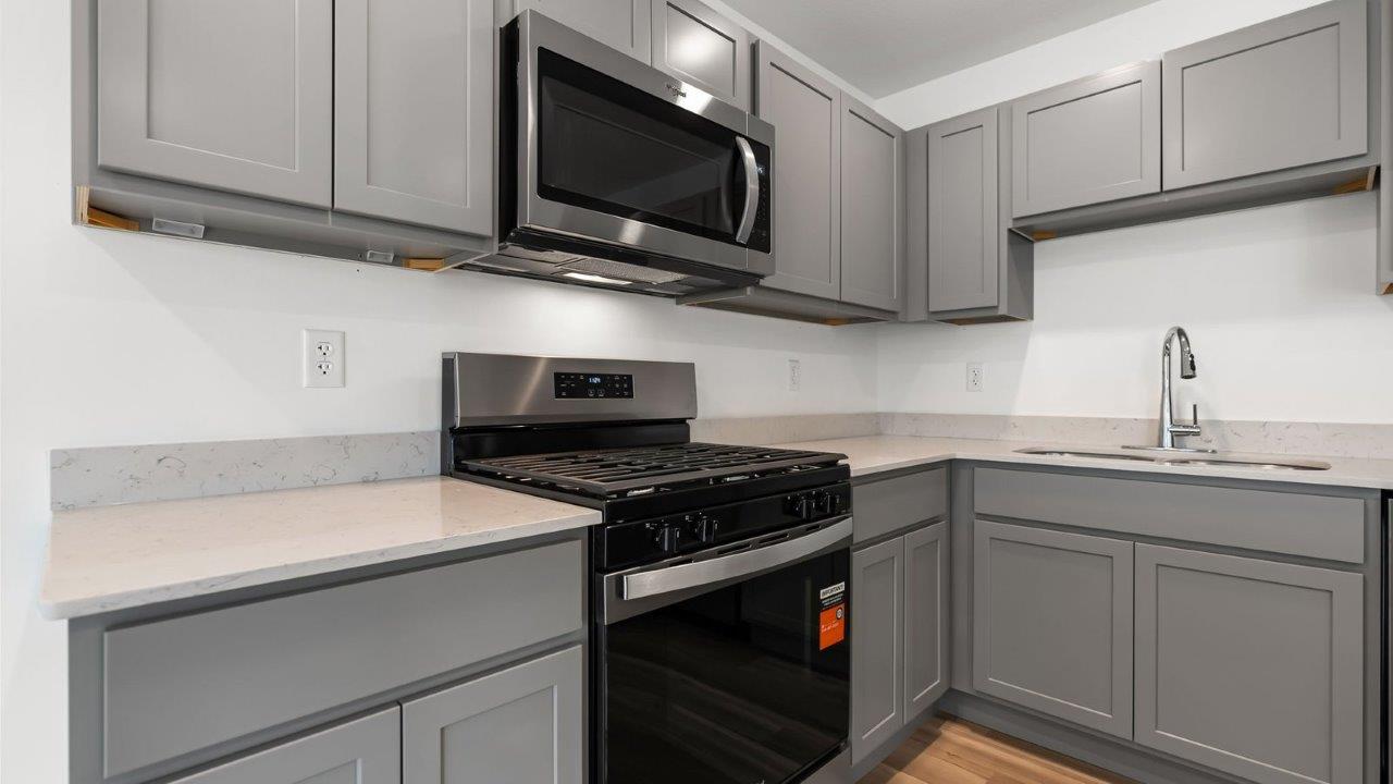 whispering pines pearson kitchen with gray cabinets, quartz countertops, lvp flooring, island with bar seating, and stainless steel appliances