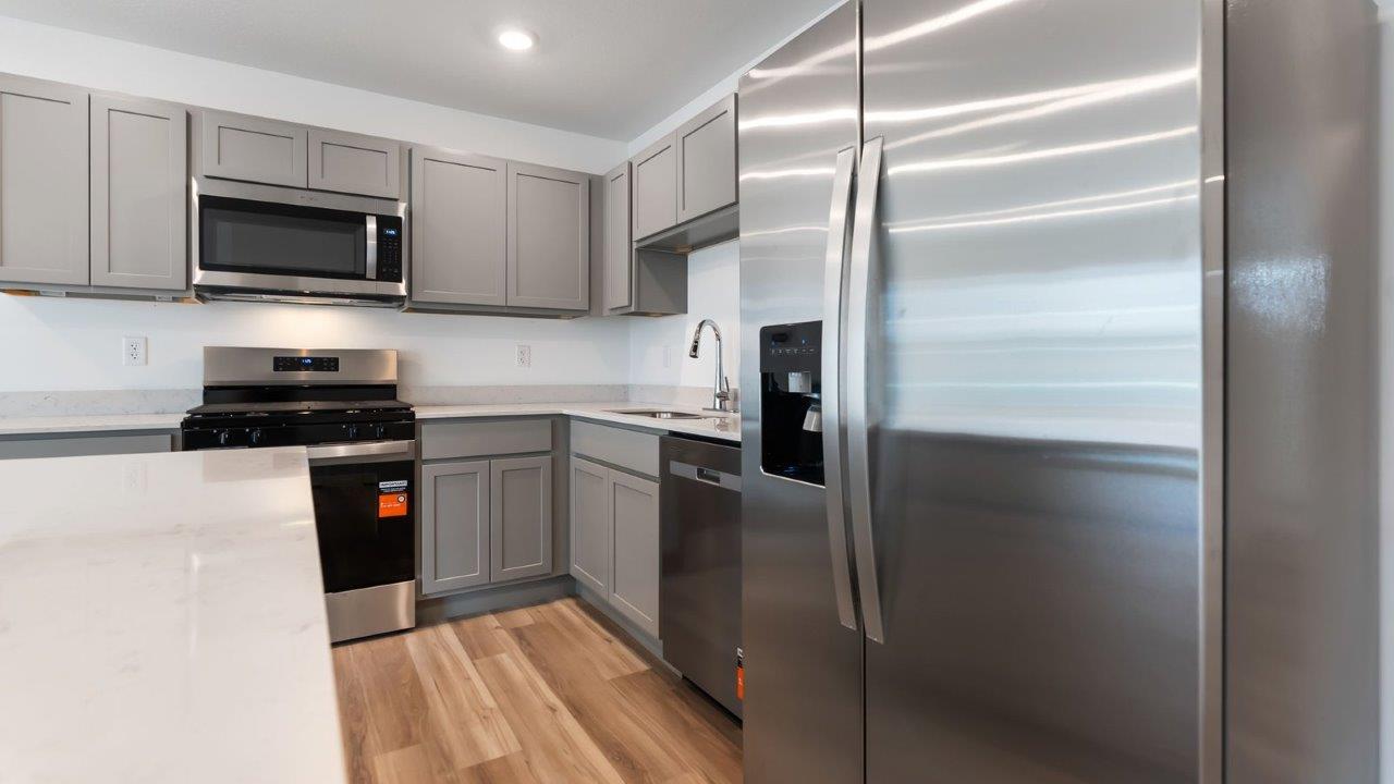 whispering pines pearson kitchen with gray cabinets, quartz countertops, lvp flooring, island with bar seating, and stainless steel appliances