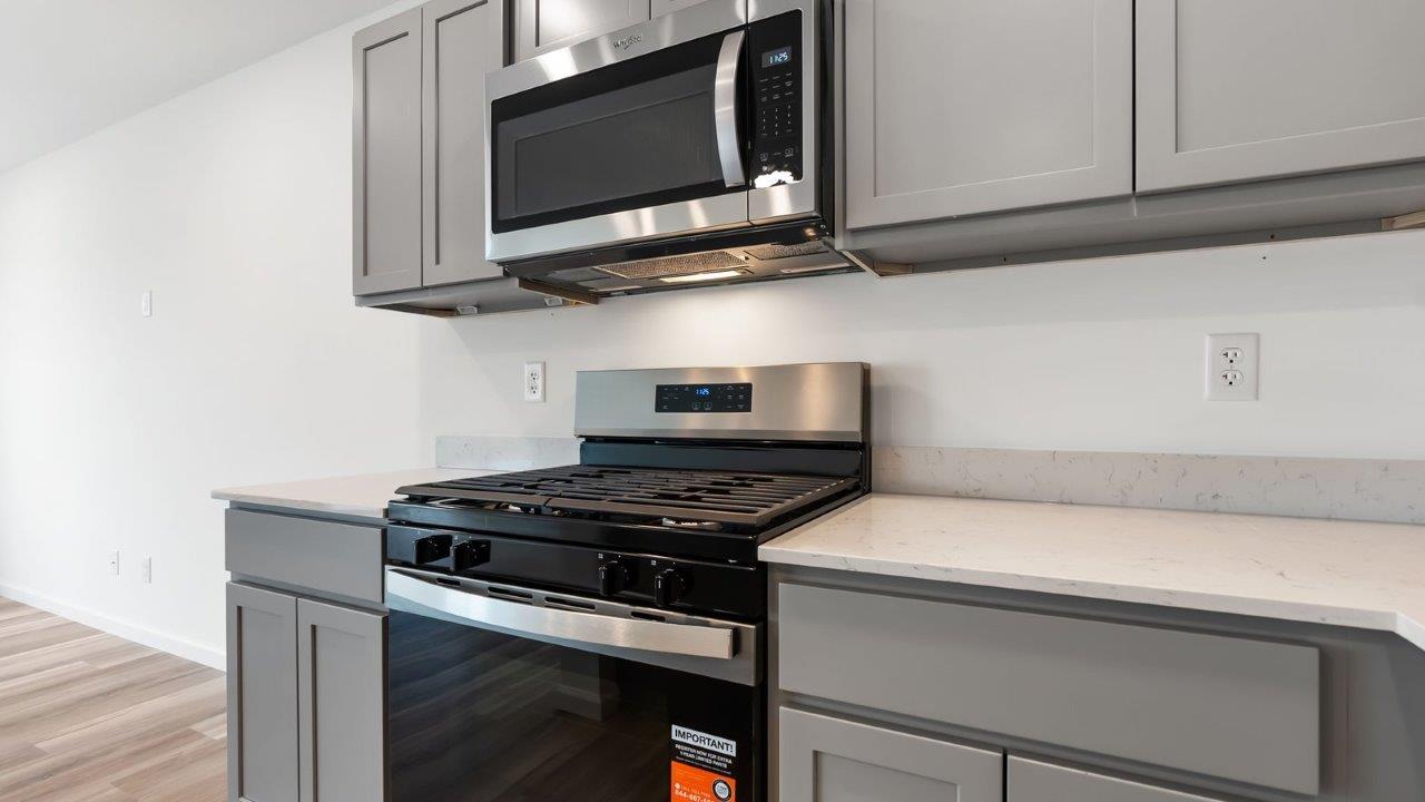 whispering pines pearson kitchen with gray cabinets, quartz countertops, lvp flooring, island with bar seating, and stainless steel appliances