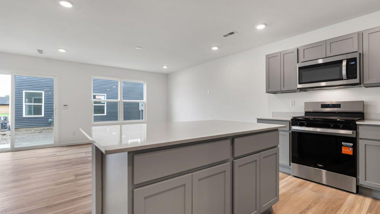 whispering pines pearson kitchen with gray cabinets, quartz countertops, lvp flooring, island with bar seating, and stainless steel appliances