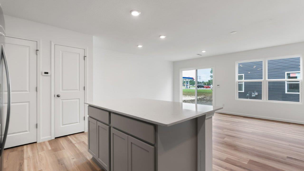 whispering pines pearson kitchen with gray cabinets, quartz countertops, lvp flooring, island with bar seating, and stainless steel appliances