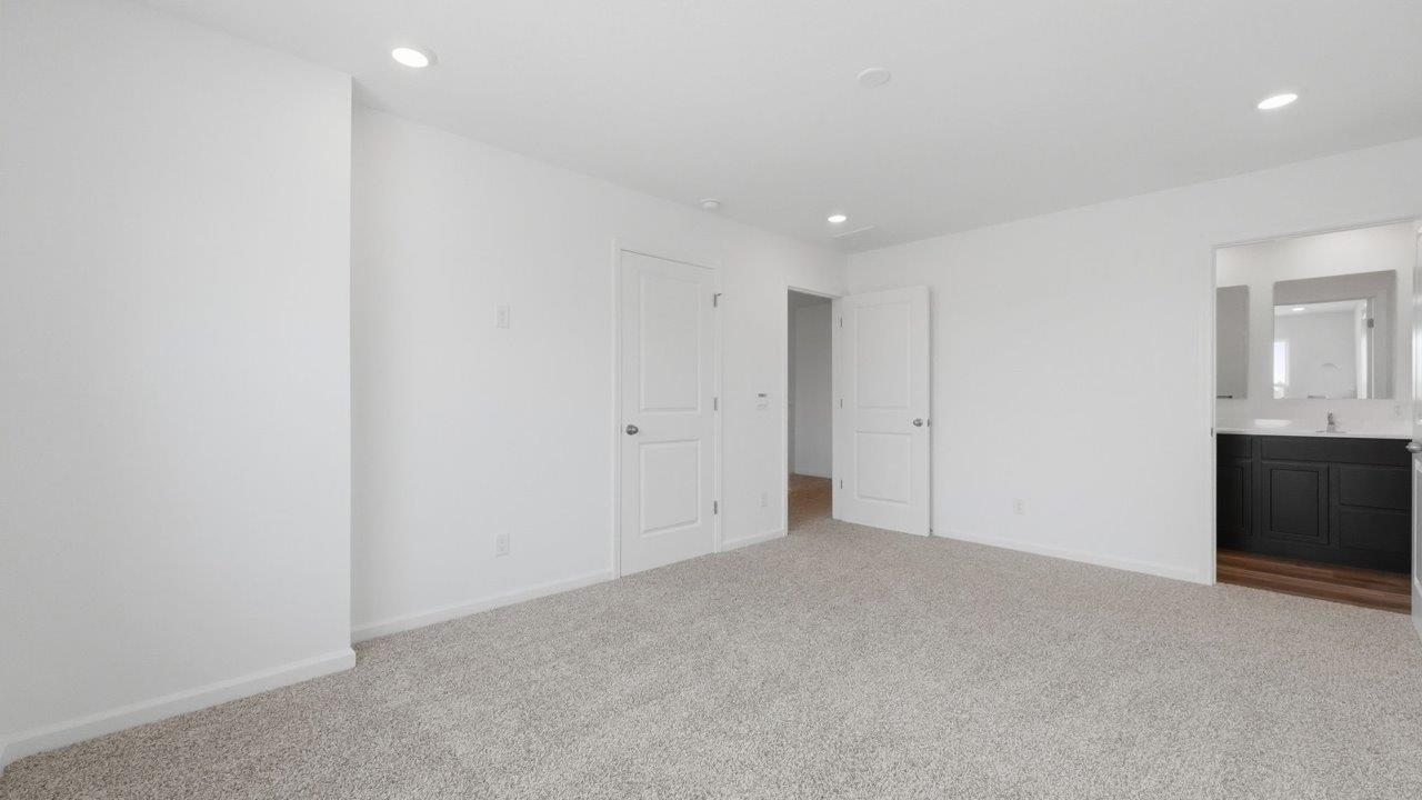 whispering pines pearson primary bedroom with beige carpet, white walls, and ensuite bathroom and walk in closet