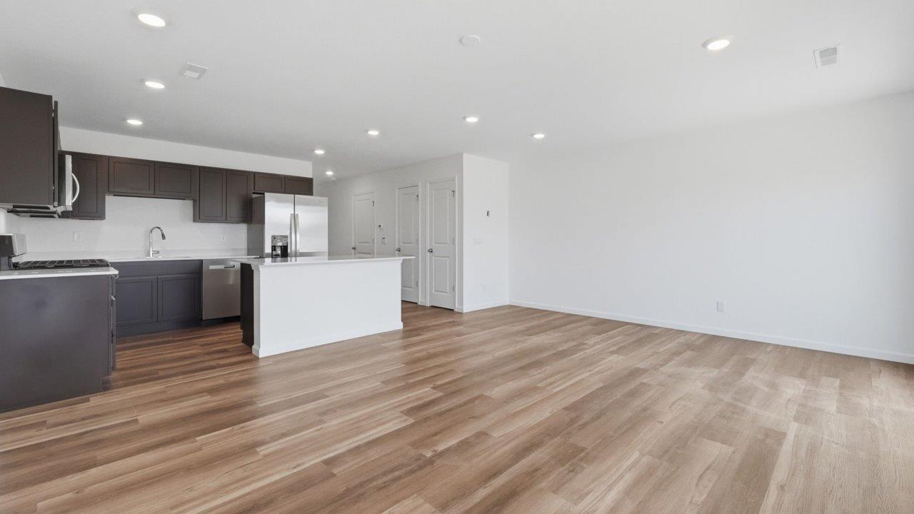 whispering pines pearson open layout kitchen with lvp flooring, sarsaparilla cabinets, stainless steel appliances, and island with bar seating