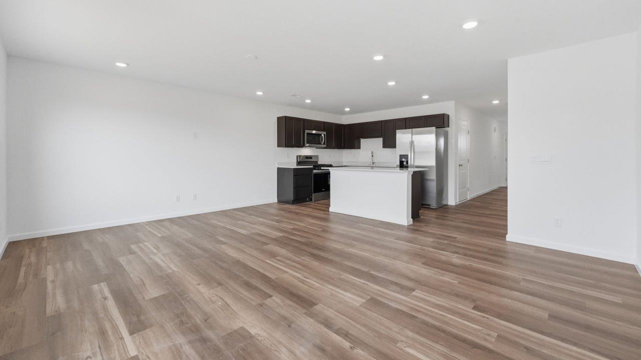 whispering pines pearson open layout kitchen with lvp flooring, sarsaparilla cabinets, stainless steel appliances, and island with bar seating